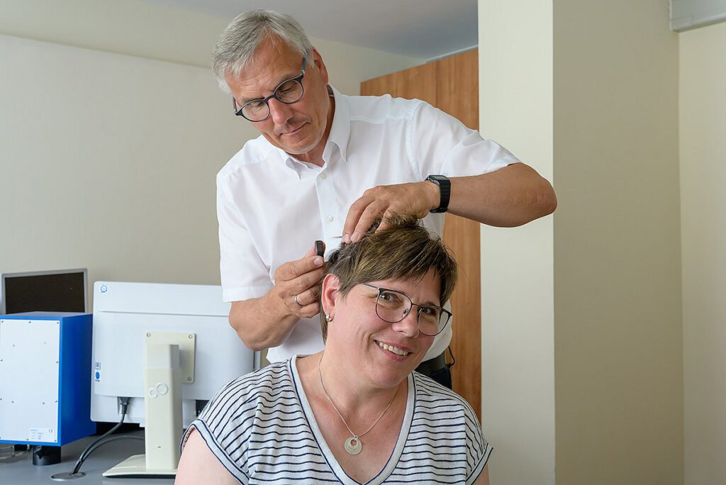 Prof. Dr. Dr. Ulrich Hoppe passt bei Patientin Elke L. den externen Sprachprozessor an. Die individuelle Einstellung des Cochlea-Implantats erfolgt im CICERO-Zentrum des Universitätsklinikums Erlangen und erfordert regelmäßige Nachsorgetermine für eine optimale Hörleistung.