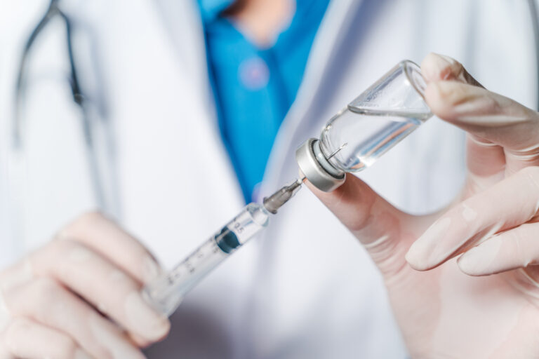The doctor holding a syringe with Covid-19 vaccines in glass bot