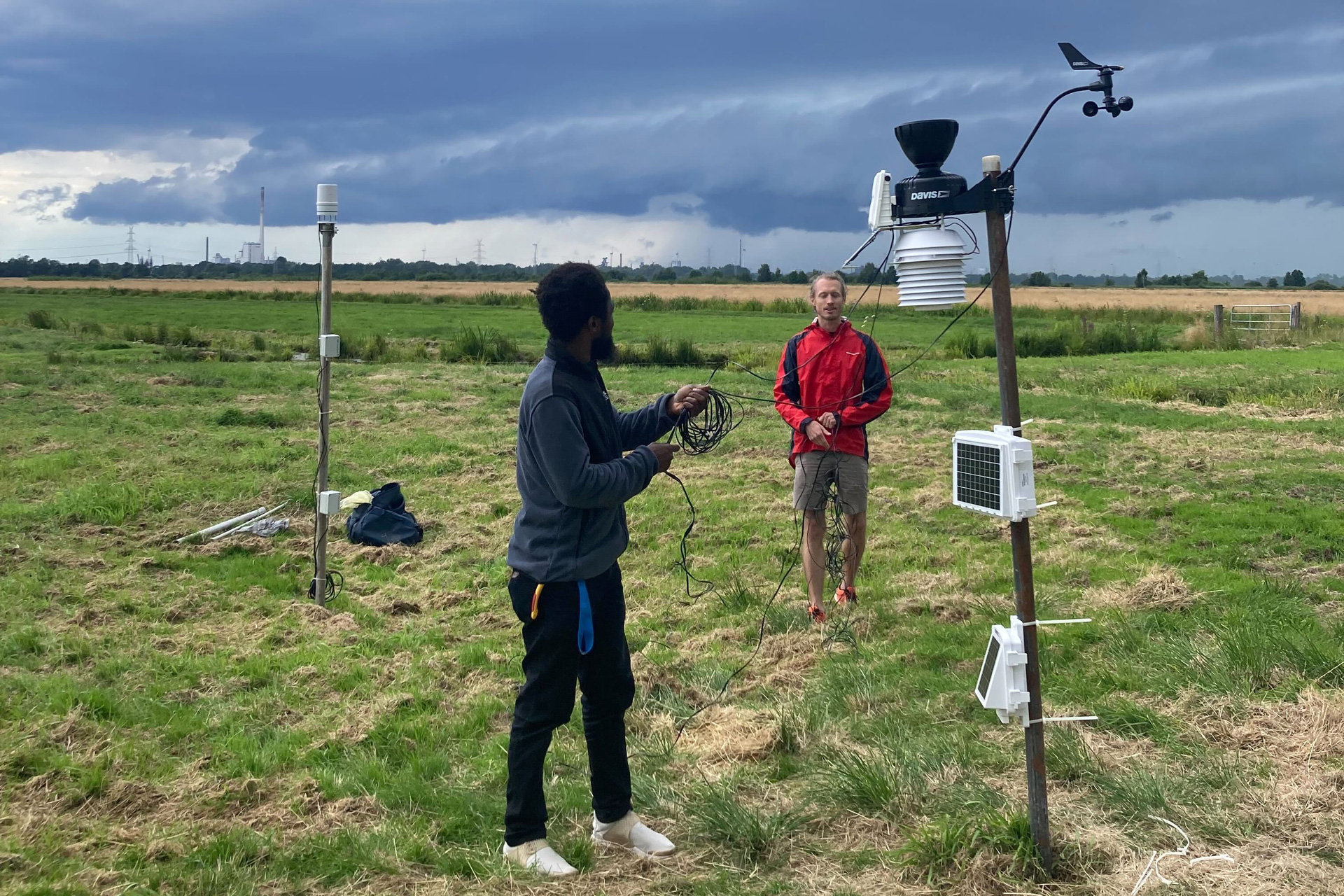 Installation von Wetterstationen durch die Arbeitsgruppe (links: Yahaya Bashiru, rechts: Maxime Colin), mit einem sich annähernden Gewitterwolken-Cluster im Hintergrund. © Irene Livia Kruse