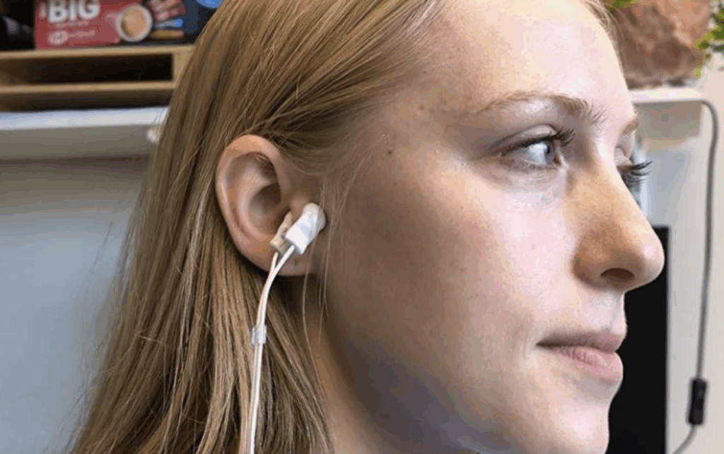 Ein kompaktes, weißes Stimulationsgerät sitzt am Ohr und sendet gezielte Impulse über die Haut. © UCL