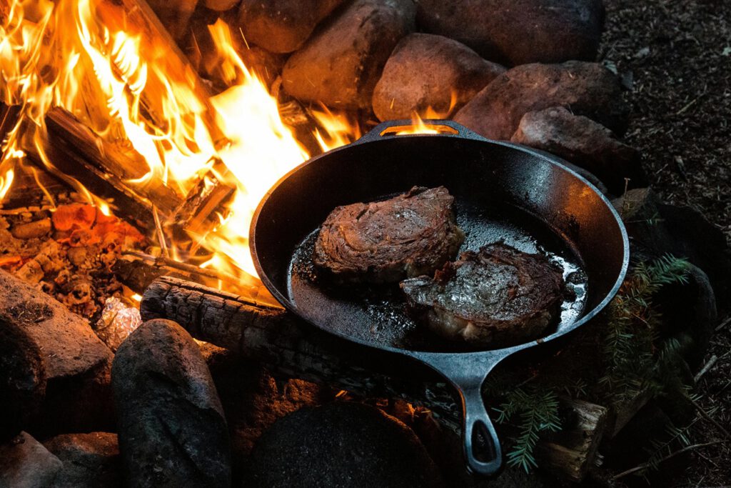 Fleisch wird in einer Pfanne über dem Feuer gebraten