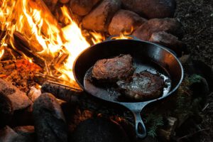 Fleisch wird in einer Pfanne über dem Feuer gebraten