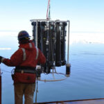 Ein Mann in Arbeitskleidung und Helm zieht ein Messgerät aus dem Meer.