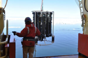 Ein Mann in Arbeitskleidung und Helm zieht ein Messgerät aus dem Meer.