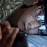 Junge liegt mit Smartphone im Bett