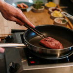 Mann brät Fleisch in einer Pfanne