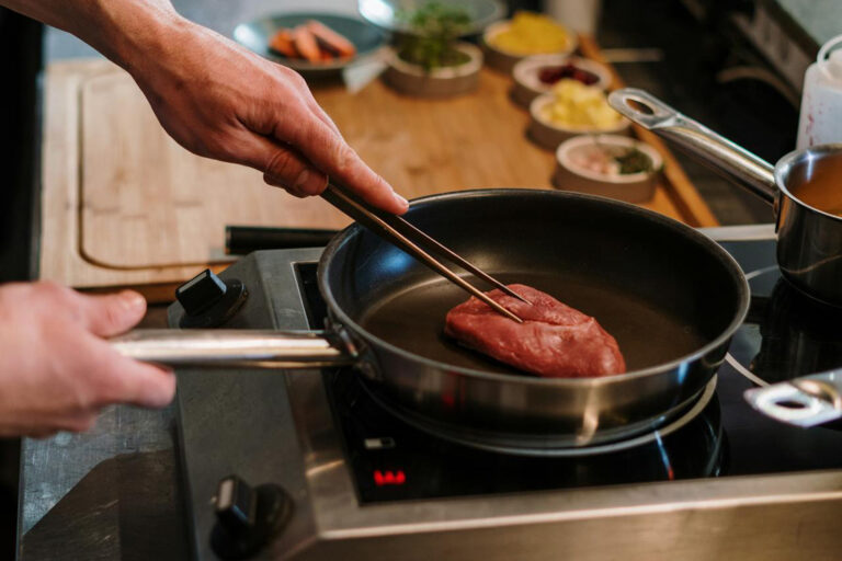 Mann brät Fleisch in einer Pfanne