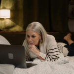 Ältere Frau liegt nachts im Bett und schaut auf ihren Laptop