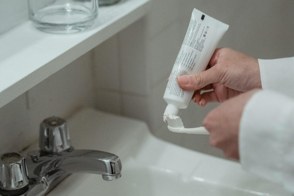 Frau macht Zahnpasta über einem Waschbecken auf die Zahnbürste