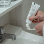 Frau macht Zahnpasta über einem Waschbecken auf die Zahnbürste