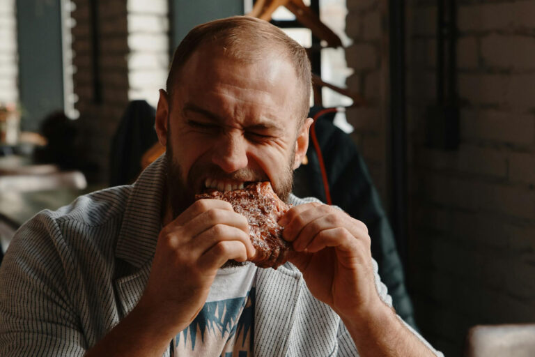 Mann beißt in ein Stück Fleisch