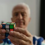 Zwei Hände lösen einen Zauberwürfel, im Hintergrund ist verschwommen der alte Mann zu sehen, der den Würfel hält.