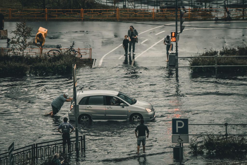 Eine überflutete Straße, ein Mann schiebt ein Auto durch das Wasser.