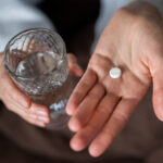 Frau hält ein Glas Wasser und eine Tablette in der Hand