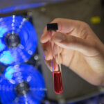 Eine Hand hält ein Reagenzglas mit einer rötlichen Flüssigkeit.