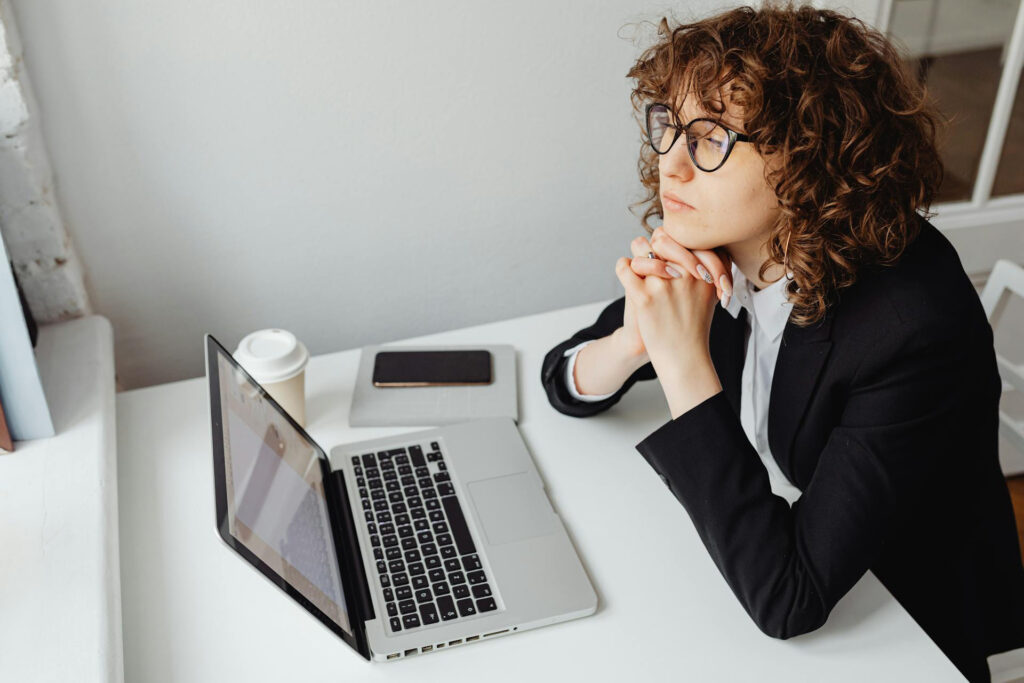 Junge Frau sitzt vorm Laptop und schaut verträumt
