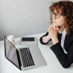 Junge Frau sitzt vorm Laptop und schaut verträumt