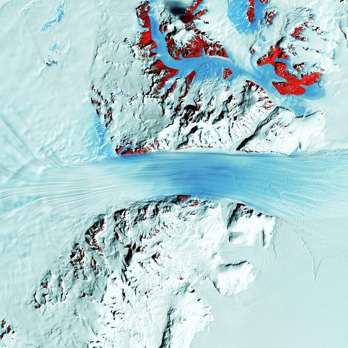 Der Byrd-Gletscher fließt schnell durch das Transantarktische Gebirge – vom Polarplateau zum Ross-Schelfeis. In der Infrarotaufnahme markieren rote Flächen freiliegendes Gestein; laut Forschern half die Hebung der Berge, den Eisschild wachsen zu lassen. © United States Geological Survey