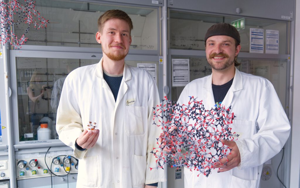 Lasse Wegner (links) und Kalle Mertin zeigen, woran sie arbeiten: eine Testzelle zur Wassergewinnung aus Luft und ein Modell des hochporösen MOF-Materials, das zugleich für effizientere Kühlung optimiert wurde. © Christina Anders, Uni Kiel