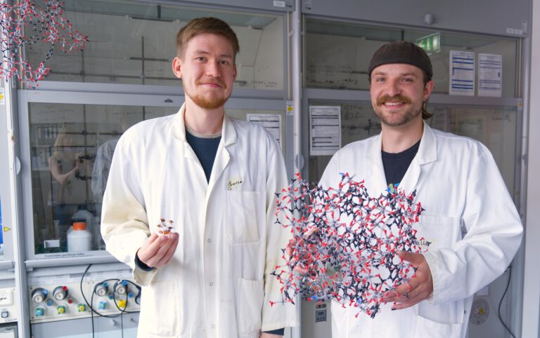 Lasse Wegner (links) und Kalle Mertin zeigen, woran sie arbeiten: eine Testzelle zur Wassergewinnung aus Luft und ein Modell des hochporösen MOF-Materials, das zugleich für effizientere Kühlung optimiert wurde. © Christina Anders, Uni Kiel
