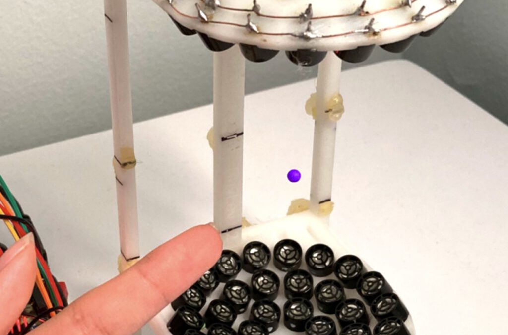 Ein neuer Zeitkristall schwebt auf einem Polster aus Schall: Das Bild zeigt ein Teilchen, das in einem 15 Zentimeter hohen, 3D-gedruckten Aufbau von Lautsprechern in der Luft gehalten wird.