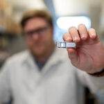 Mann hält Implantat in die Kamera