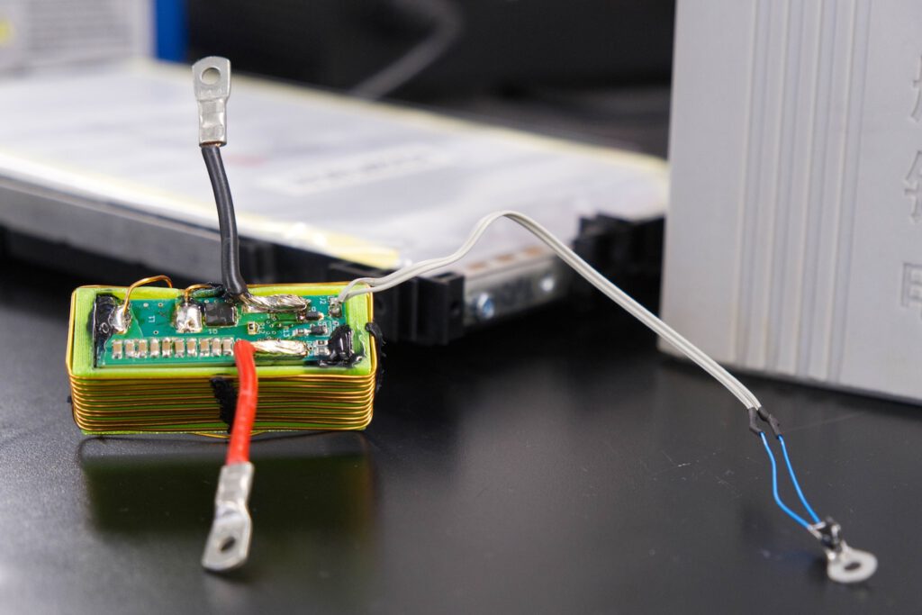Die grüne Platine enthält den elektronischen Schaltkreis, mit dem die Forschenden Sensordaten über die vorhandenen Stromanschlüsse einer Batteriezelle übertragen. Die Batteriezelle befindet sich im Hintergrund. © Christina Anders, Uni Kiel